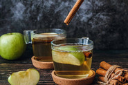 Green apples and cinnamon sticks falling into two cups of apple tea; Photo by Pexels, Tijana Drndarski 
