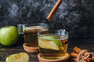 Green apples and cinnamon sticks falling into two cups of apple tea; Photo by Pexels, Tijana Drndarski